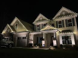 Elegant estate with warm white holiday lighting on hedges and roofline