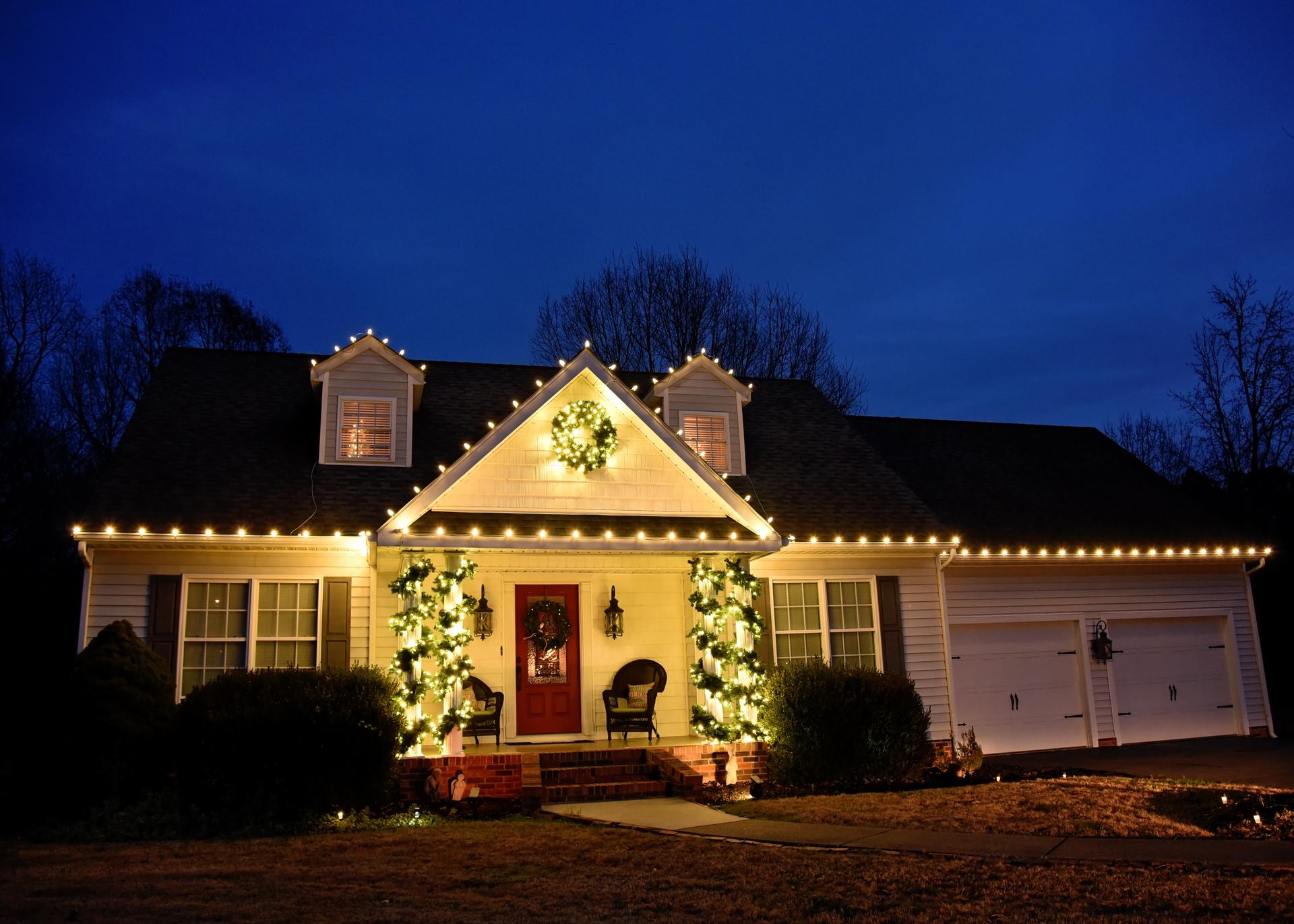 Soft white Christmas lights on colonial home with manicured hedges